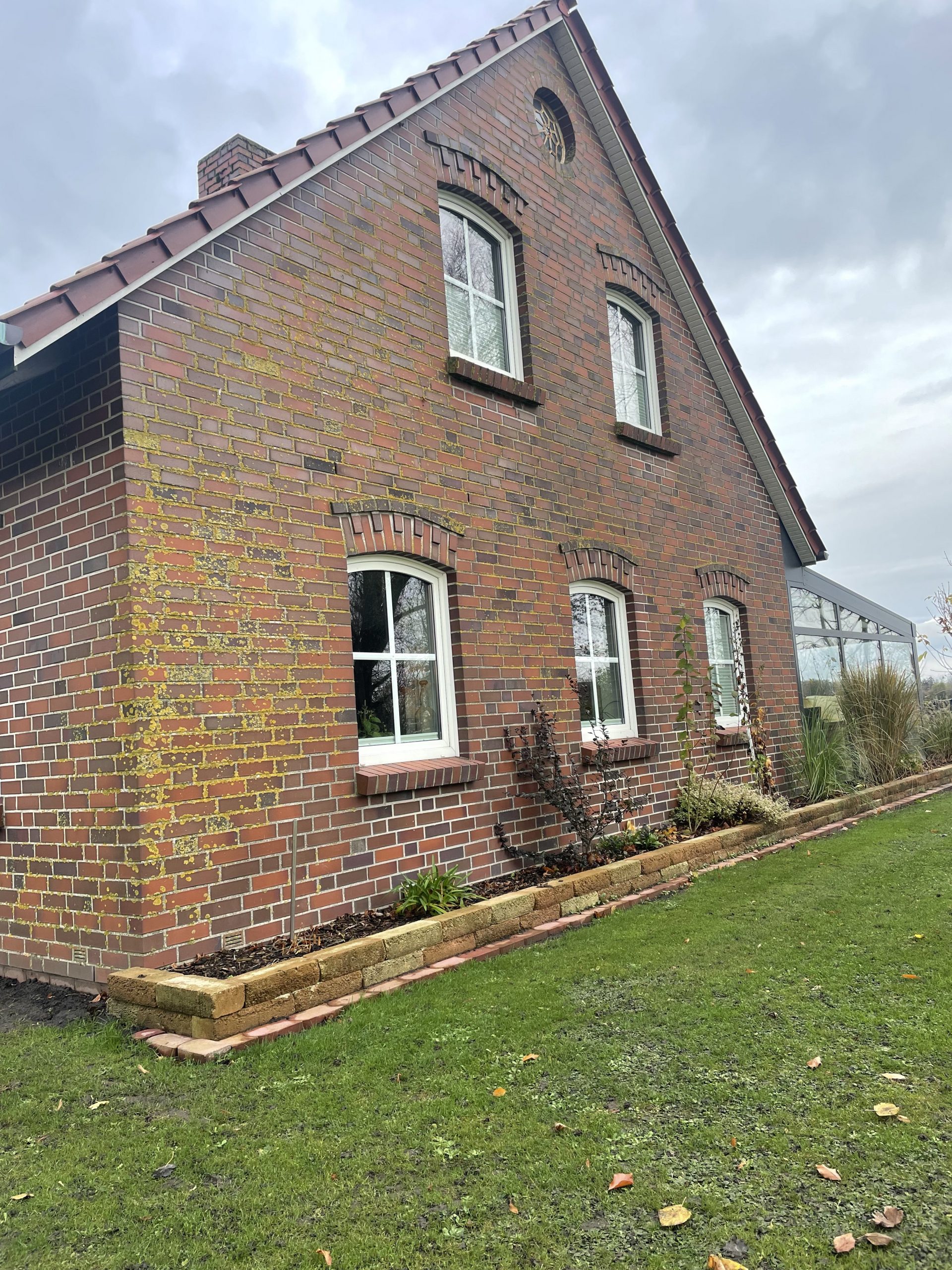 Ziegelhausfassade vor der Reinigung, mit deutlichen Verschmutzungen durch Algen und Flechten auf den Ziegeln und Fugen